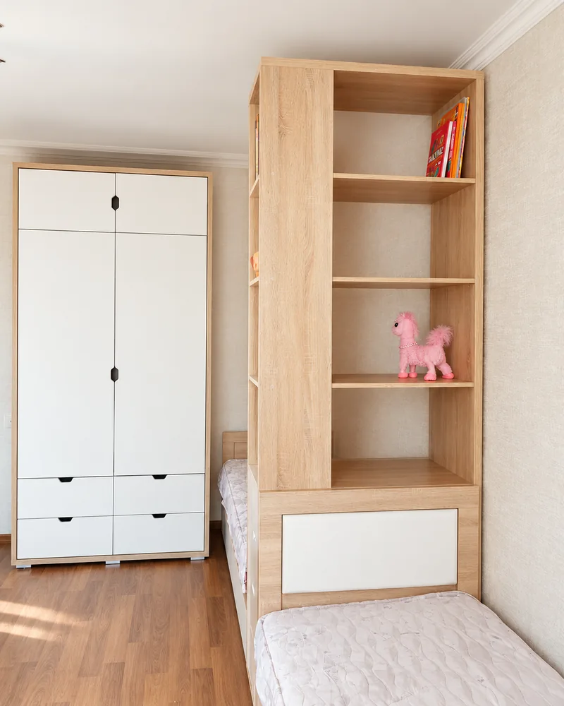 Светлый стеллаж у детской кровати и белый шкаф с ящиками